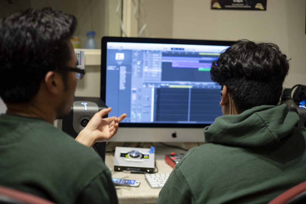 From behind: student and teaching artist look at a music project in Logic on a computer screen and talk about the composition.