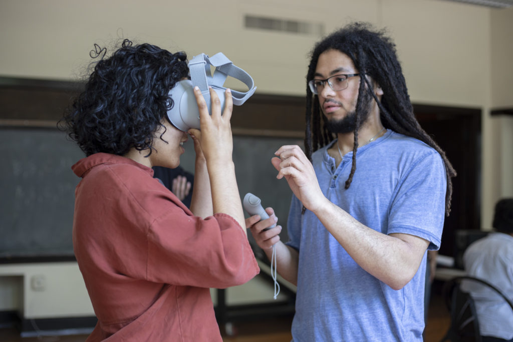 Student helps an Arts Corps staff member put on the VR headset to view the experience.