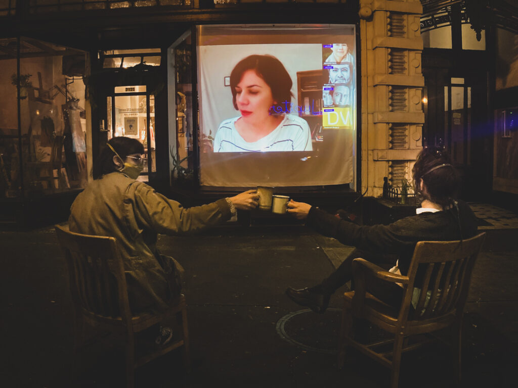Sepia photo of artists Dani Hopple and Whitney Bashaw, watching a regular color projection on a movable screen outside CAM