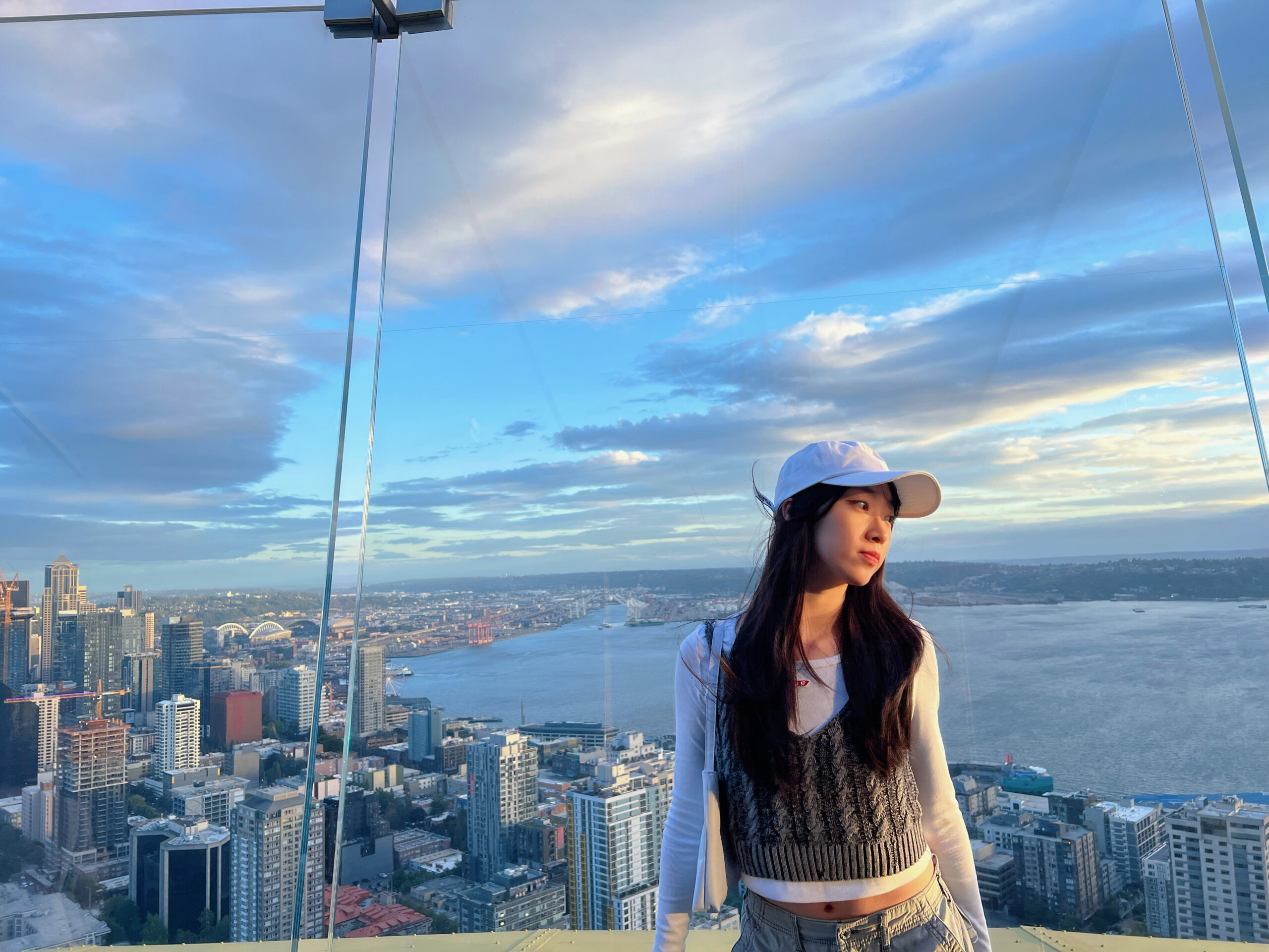 A Chinese woman in her 20s, Angela, looks off to one side with the skyline of Seattle behind her