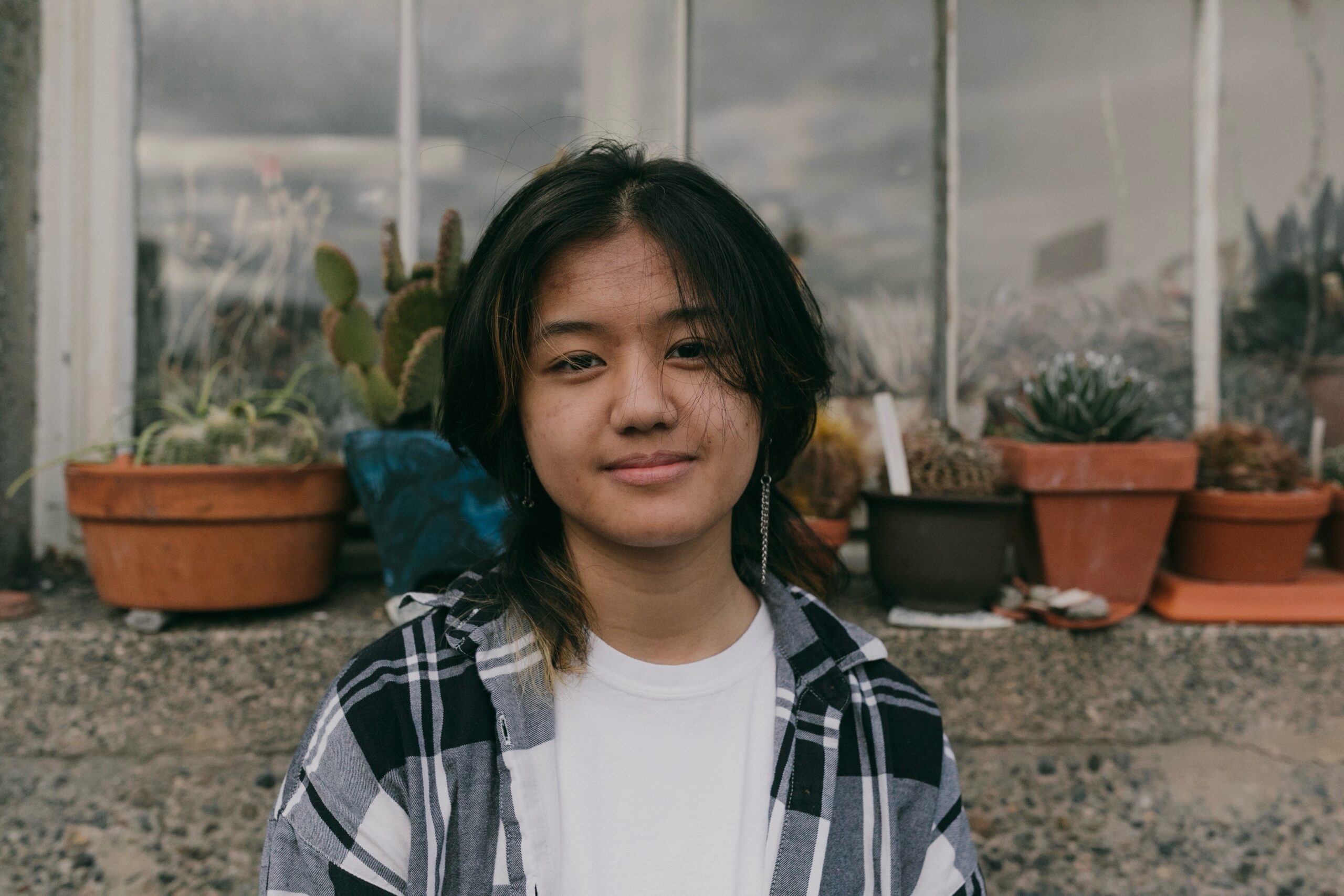 Student Mica Viacrucis, a teenager with dark shoulder-length hair, wearing a flannel in front of potted succulents