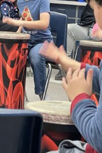 The hands of students as they drum on tubing drums sited in a classroom