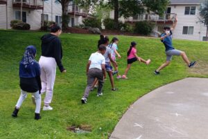 Teaching artist leads a line of youth skipping in a lawn in an apartment complex