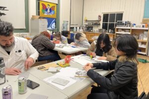 The Arts Corps office, with white tables in shape on "L", students and teaching artist Adam working on art