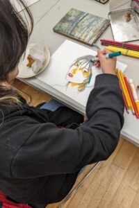 A teenage student works on a drawing of a face with markers