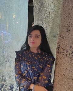 Photo of Shreya, an Indian woman with long hair wearing a flowery blouse, leaning against stone pillars