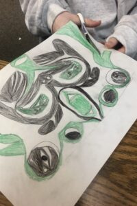 Hands of a student cutting up a black and green design in the style of Coast Salish art