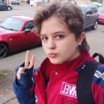 Selfie of Atticus Sweat, a young man with blond curly hair wearing a red and blue Marvel jacket, holding up a peace sign