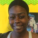 Headshot of Maryem, a black young woman with her hair under a cap, wearing hoop earrings. Bright yellow background