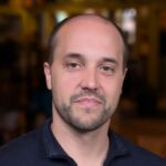 Headshot of Jason Ehlenfeldt, a man in his 30s with a trim beard and balding, short hair, wearing a blue collared shirt