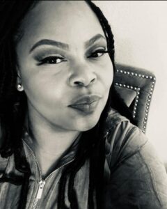 Black and white selfie of Erica, a black woman with long black hair and lashes, wearing a hoodie