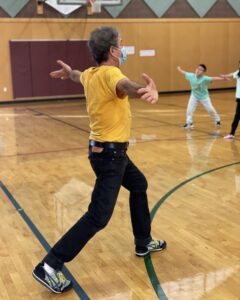 A Brazilian man with curly salt-and-pepper hair in a lounge position with his arms outstretched