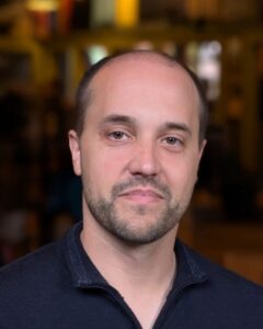 Headshot of Jason Ehlenfeldt, a man in his 30s with a trim beard and balding, short hair, wearing a blue collared shirt