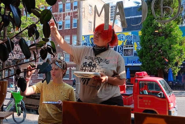 Photo through a window as two high school students paint letters on it.